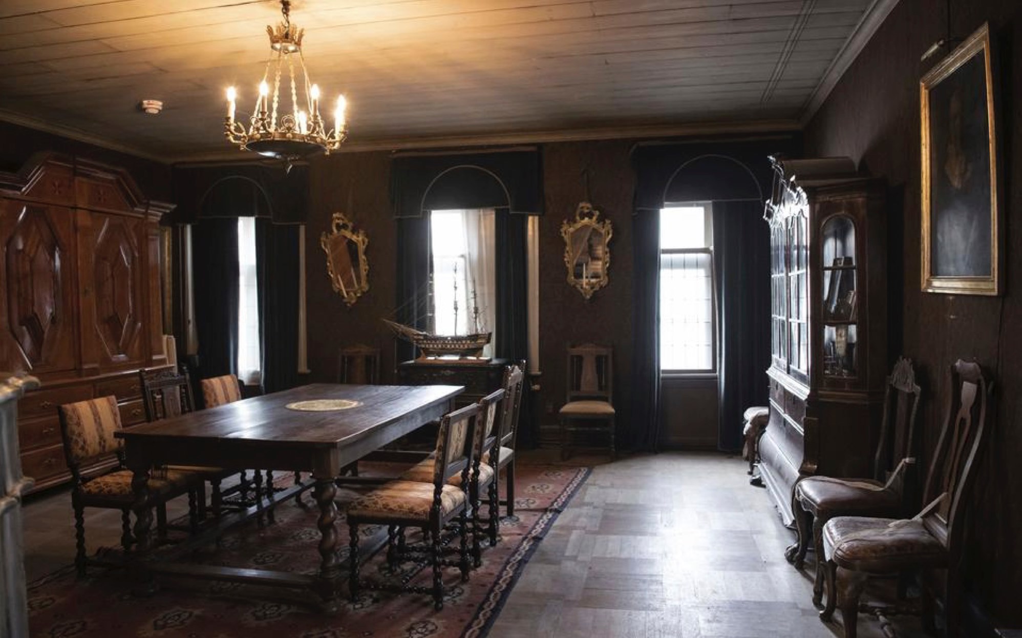 Kungssalen Kungasalen at Gathenhielmska Huset. The room features a wooden table, chairs, cabinets, mirrors and a portrait painting in a glass frame.